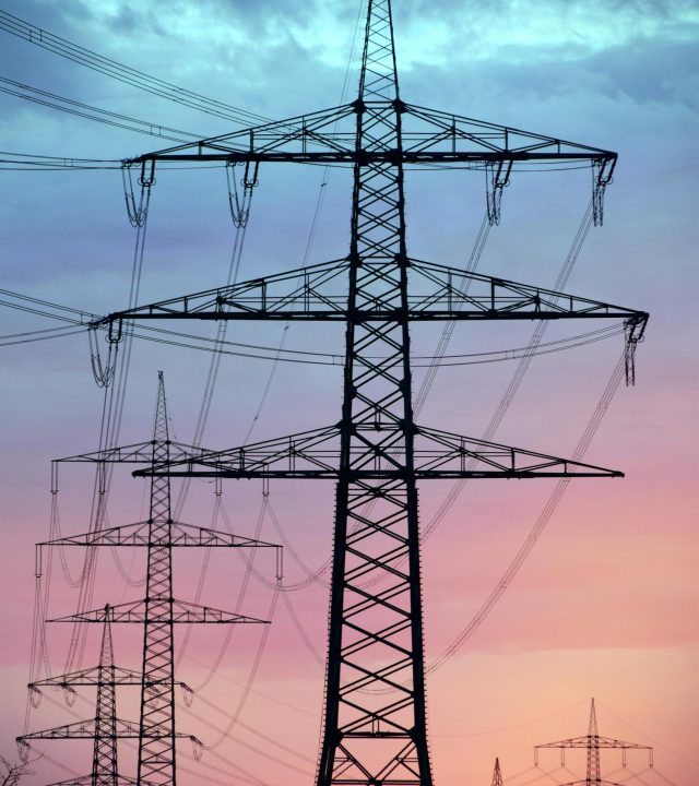Electricity pylons silhouetted against a dramatic sunset sky, showcasing high voltage transmission.